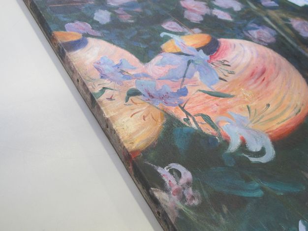 Colour photograph. Detail view of the edge of a painting showing paper lanterns in a garden with white lilies. The painting continues on the canvas as the latter wraps around the wooden stretcher beneath.