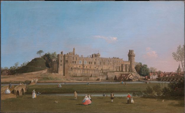 Painting. A crenelated, brown stone castle with a tower at the right end stretches across the middle ground in this wide landscape. Men wearing suits and hats and women wearing long dresses with full skirts walk or stand along the grassy lawn on our side of narrow river. Children and dogs enliven the scene.